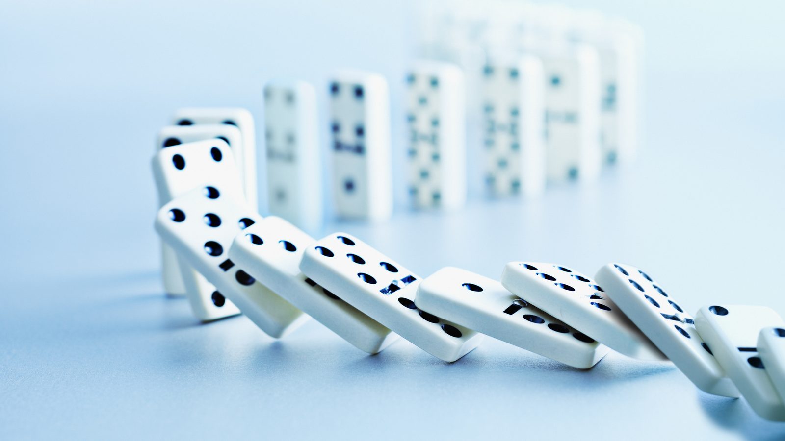 A row of white dominoes toppling on a blue surface reflecting the testing that catches problems before a localized course launches